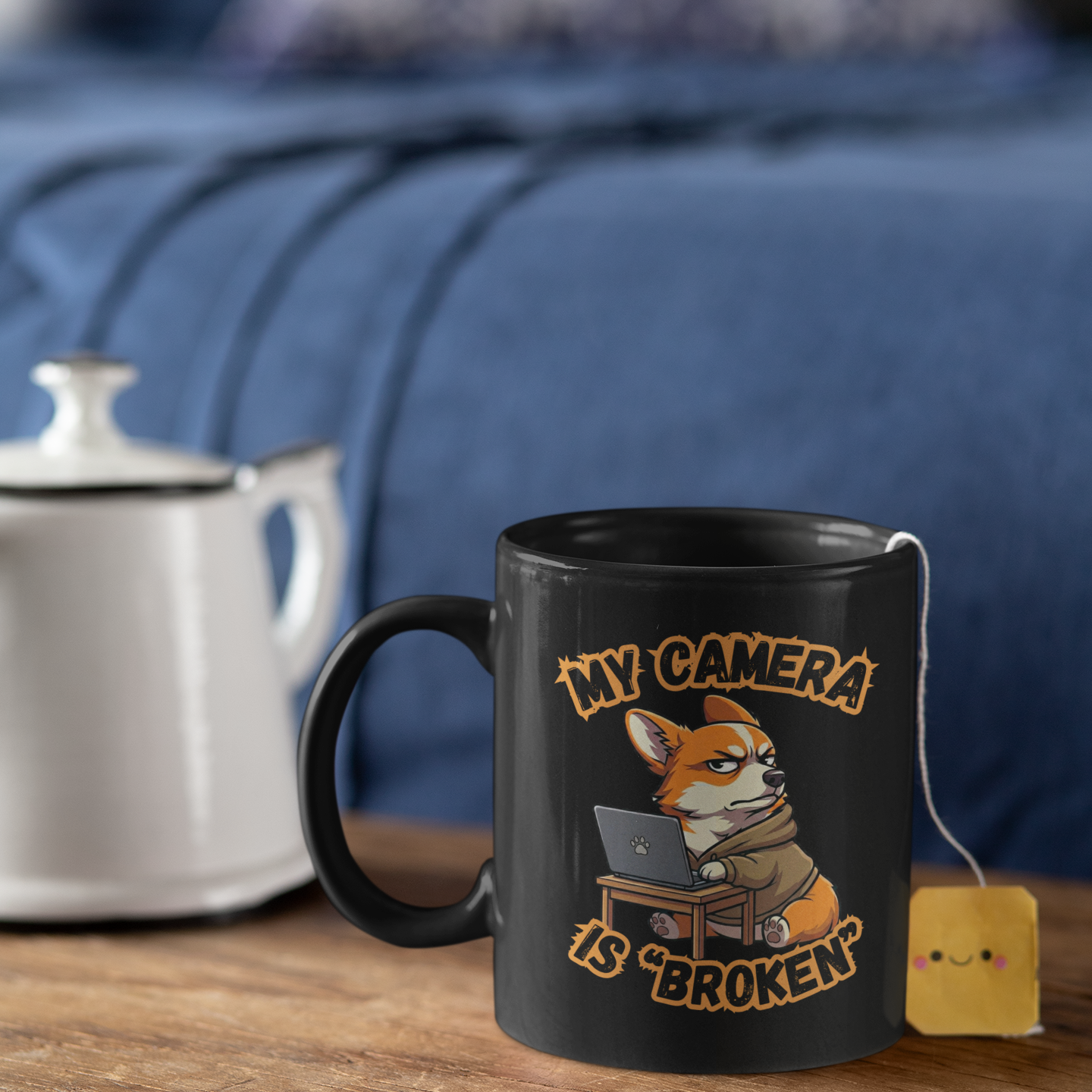 Black mug with a fox graphic and text on a wooden surface with a teapot and tea bag.
