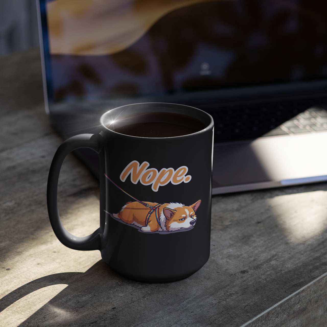 Black mug with a dog illustration and 'Nope' text on a wooden table with a laptop in the background.