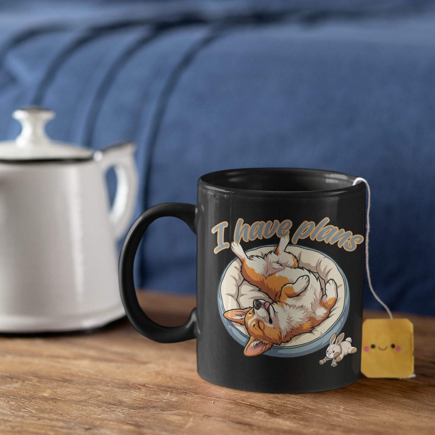 Black mug with fox design and 'I have plans' text on a wooden surface with a teapot and tea bag.