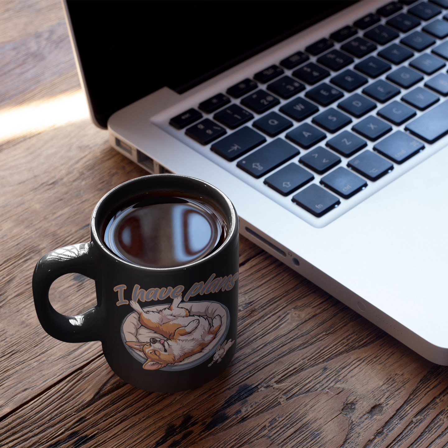 Black mug with a design and text next to a laptop on a wooden surface
